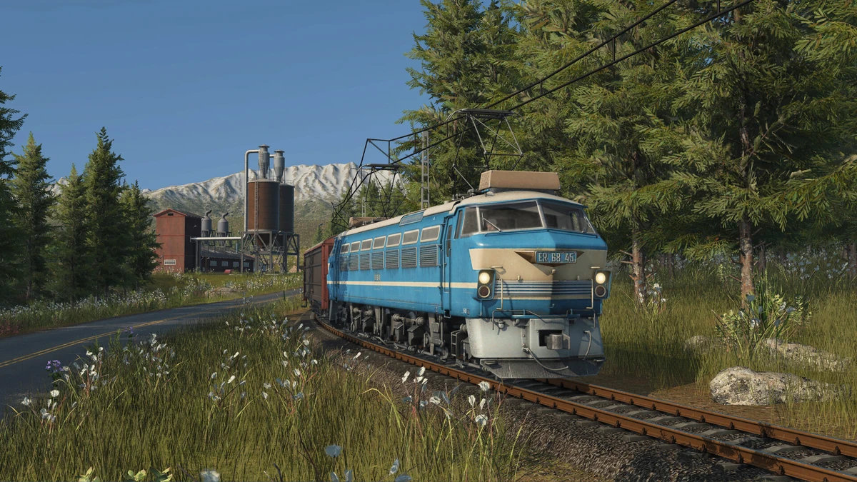 รถไฟสีฟ้าวิ่งบนรางใกล้ป่าและอาคารอุตสาหกรรม